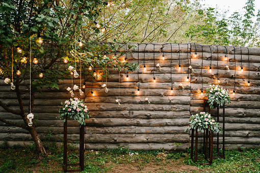 Wooden wall decorated garland with luminous bulbs and electric lamps decorated flowers. Original wedding floral decoration.  Wedding. Reception. Lounge zone.