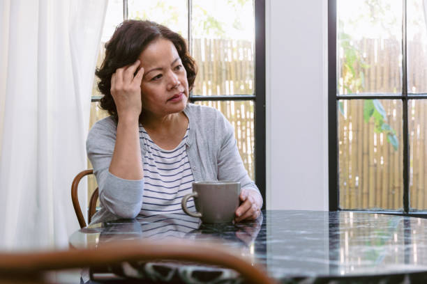 Emotionally stressed senior woman Upset senior woman drags her hand through her hair while staring out the window in her home. She is sitting at the kitchen table. A coffee cup is in front of her. breakfast room photos stock pictures, royalty-free photos & images