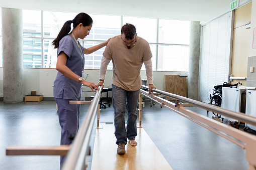 Male patient takes first steps using orthopedic parallel bars
