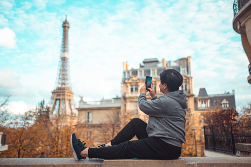 an asian chinese female traveller taking photo in front of famous place eiffel tower during day time