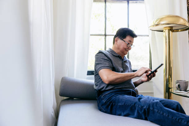 istock Senior man uses smartphone while relaxing on sofa 1184637898