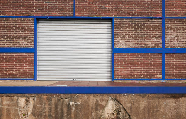 istock Silver rolling garage door and brick wall with blue pillars 1184642200