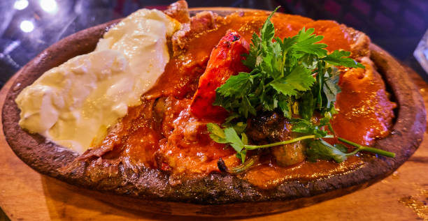 istock Iskender Kebap, grilled meat from a spit with soaked Turkish flat bread under a thick layer of tomato sauce with a large splash of yoghurt, garnished with parsley on a clay plate 1184642517