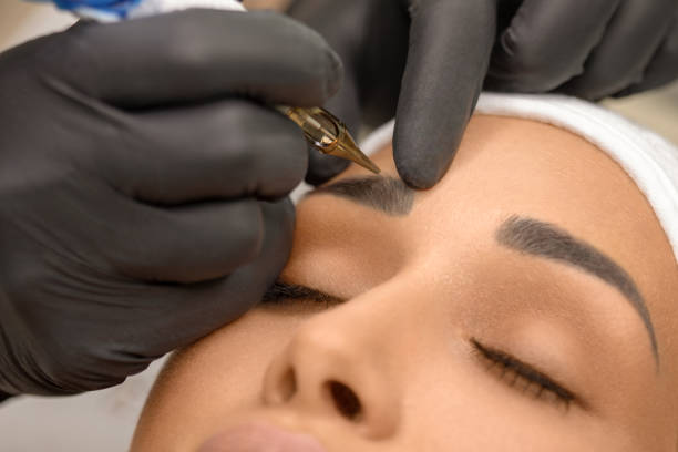 Beautiful young woman receiving permanent make up Make up artist applying permanent make up on eyebrows at beauty treatment. Beautician contouring and shading young woman's eyebrow with special tool. eyebrow stock pictures, royalty-free photos & images