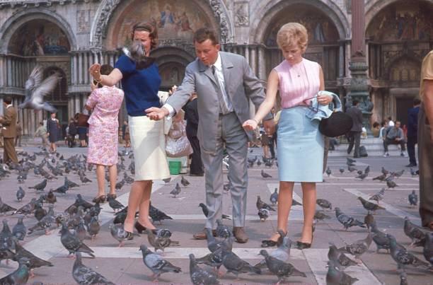 Venice, Venzien, Italy, 1966. Tourists feed pigeons on the St. Marcus square in Venice. Also: St. Mark's Cathedral.