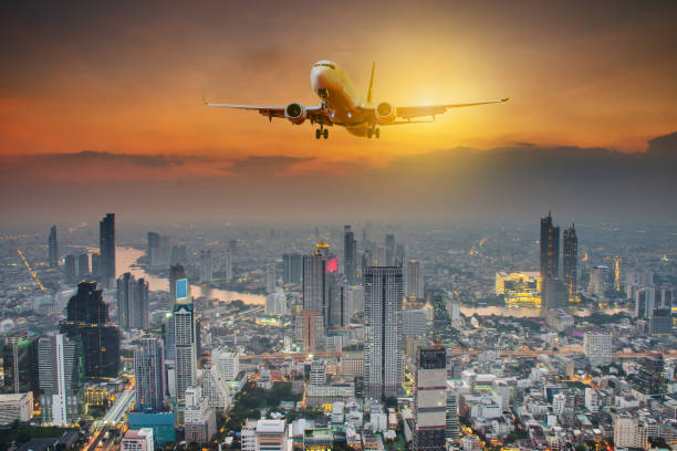 istock Panoramic view over the evening city during sunset, and White passenger plane flying in the sky above a city 1184647748