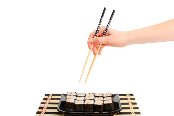 Sushi set with red fish, a cucumber and shrimps on a black plate Sushi set with red fish, a cucumber and shrimps on a black plate. The female hand takes sushi. The girl's hand on a white background with Japanese chopsticks. kids eating tuna stock pictures, royalty-free photos & images