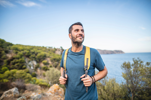 Fit male backpacker in early 30s looking away from camera before continuing along Mediterranean coastal trail.
