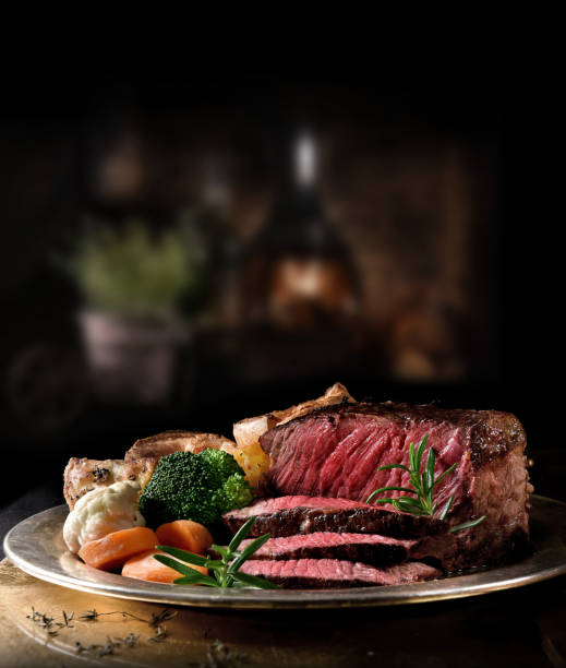 Rustic Rare Roast Beef Succulent side of rare roast beef with seasonal vegetables, Yorkshire Puddings and roast potatoes with Rosemary garnish shot in a rustic setting with an old fashioned wood burner. Copy space. roast dinner stock pictures, royalty-free photos & images