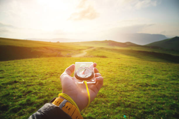 Male hand with a magnetic compass ea against the backdrop of a beautiful landscape at sunset. stock photo