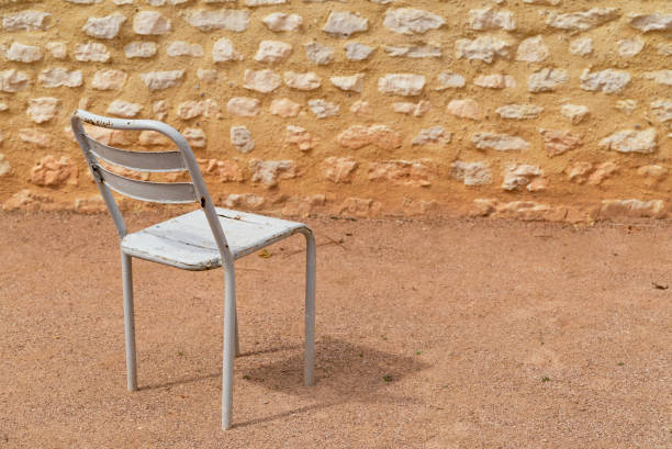 An empty white metal chair in a sandy courtyard with a rock wall
