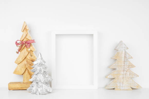 Mock up white frame with wooden Christmas tree decorations on a shelf against a white wall Mock up white frame with wooden Christmas tree decorations on a shelf. Portrait frame against a white wall. white shabby chic desk stock pictures, royalty-free photos & images