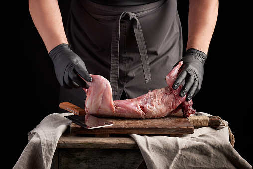 chef in black latex gloves holds a whole rabbit carcass on a brown cutting board, process of cooking meat