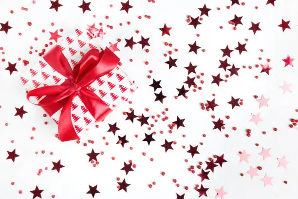 Christmas gift with red bow on white background with red stars and sparkles. Xmas template. Happy. New Year. Flat lay style.