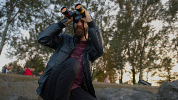 istock Young bearded man watching through binoculars the bird or something different. Coast with rocks and coast. 1184664718