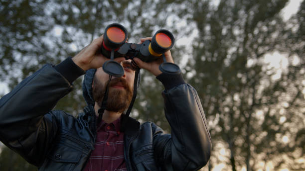 istock Young bearded man watching through binoculars the bird or something different. Coast with rocks and coast. 1184665239