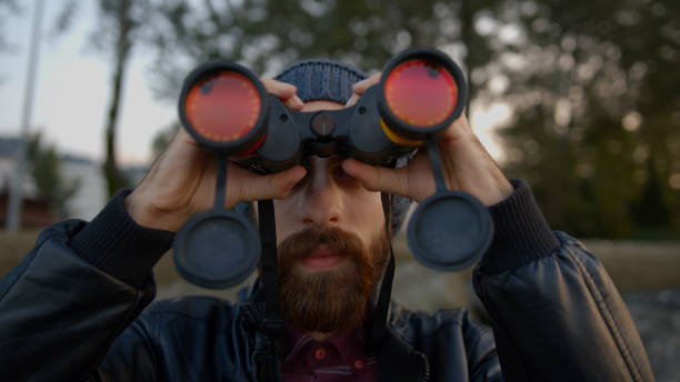 istock Young bearded hipster man with leather jacket over and with binocular with hat on his head watching bird or something different. Sea coast with rocks and seashore. 1184666717