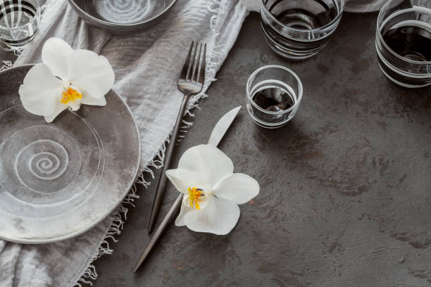 istock Elegance table setting with knitted grey napkin, cutlery, ceramic plates, glasses and white orchid flowers 1184667509
