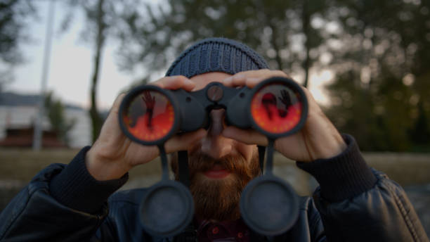 istock Young bearded hipster man with leather jacket over and with binocular with hat on his head watching bird or something different. Sea coast with rocks and seashore. 1184667595