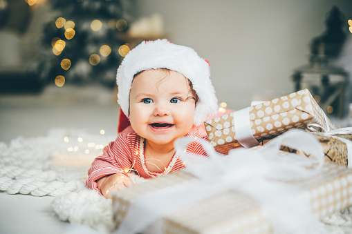 Little baby girl in Santa's hat is lying among the festive Christmas wreath.