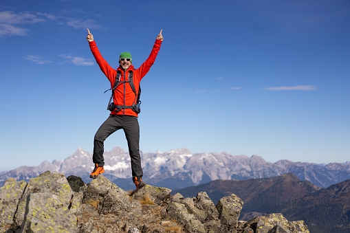 happy smiling successful mature adult man hiker mountaineer standing mountain peak both arms raised up on sunny day in autumn with beautiful mountains panorama blurred in background with place for text