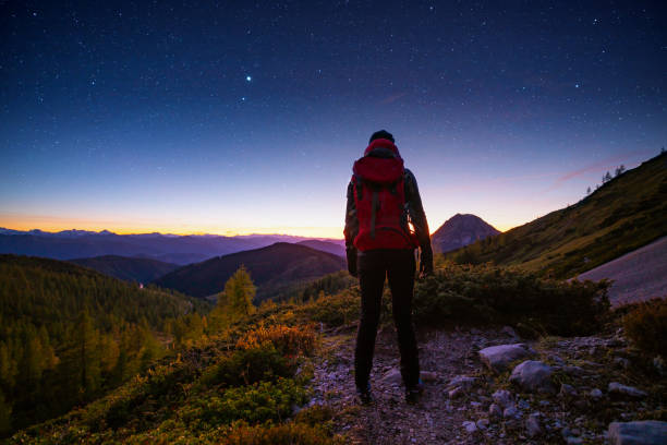 solo traveller high up in the mountains with starry heaven rear view woman hiker solo traveller with backpack standing alone in the mountains after sunset and blue hour watching starry sky blue hour twilight stock pictures, royalty-free photos & images
