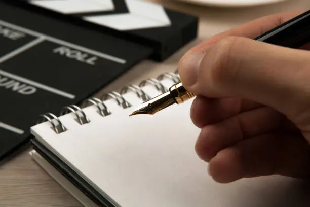 fountain pen in the hands of a screenwriter on the background of a movie clapper and a notebook