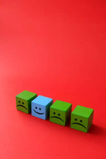 Photo of Happy and sad face emojis on wood blocks toys and red background.