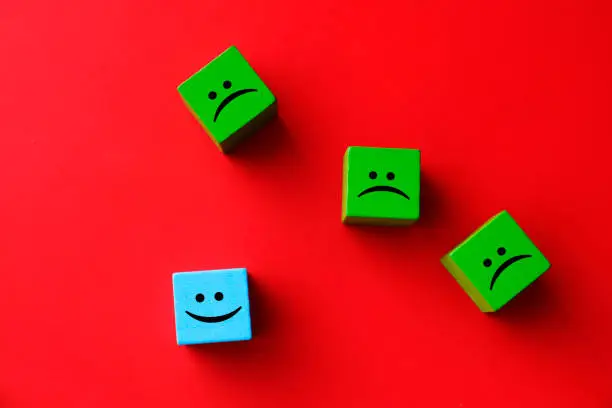 Photo of Happy and sad face emojis on wood blocks toys and red background.