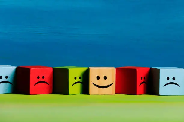 Photo of Happy and sad face emojis on wood blocks toys and color background.