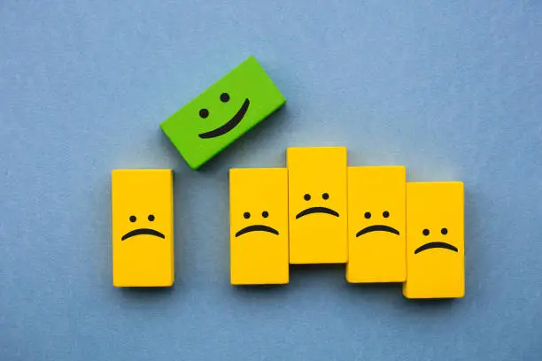 Photo of Happy and sad face emojis on wood blocks toys and blue background.