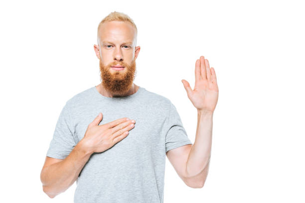 retrato de hombre barbudo serio dando un juramento con la mano arriba y la mano en el corazón, aislado en blanco - hand on heart fotografías e imágenes de stock