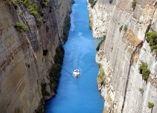 Cargo ship sails between the rocks of the Corinth Canal. Scenic summer landscape of the Corinth Canal in a bright sunny day against a blue sky with white clouds. Peloponnese, Greece