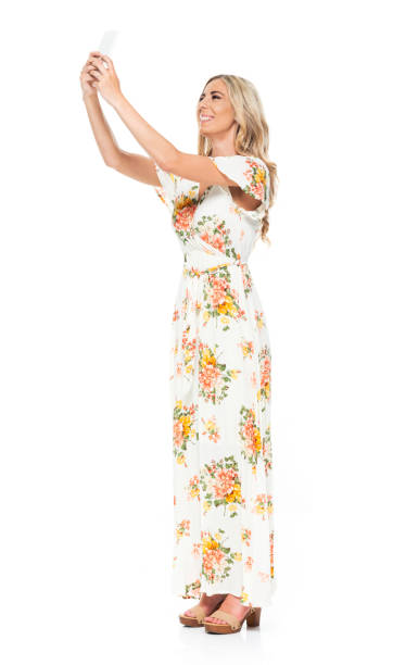 side view / profile view / full length of 20-29 years old adult blond hair / long hair caucasian young women standing in front of white background wearing dress / long dress who is smiling / happy / cheerful who is taking a selfie / photographing - 20 25 years profile female young adult imagens e fotografias de stock