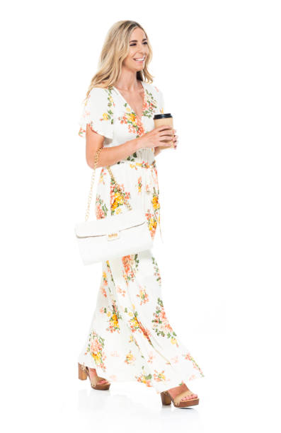 side view / profile view / full length of 20-29 years old adult blond hair / long hair caucasian young women walking in front of white background wearing dress / long dress who is smiling / happy / cheerful and holding coffee cup / purse - 20 25 years profile female young adult imagens e fotografias de stock