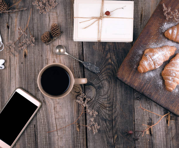 smartphone with blank black screen, brown ceramic cup with coffee and baked croissants sprinkled with icing sugar