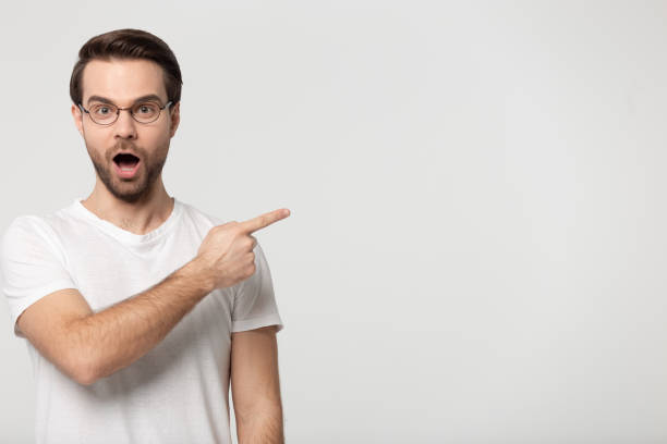 istock Excited young guy pointing finger aside on empty free space. 1184709964