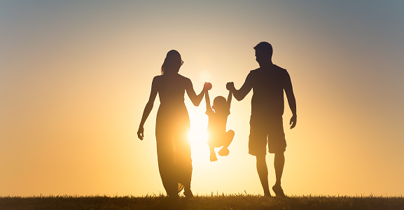 Happy family silhouette on sunset background. Father, mother, baby son run. Child jumping and playing with parents.