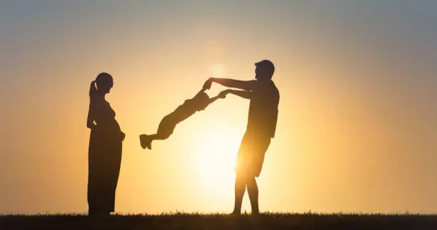 Photo of Father, mother, child son playing together in the park, having fun in nature sunset.