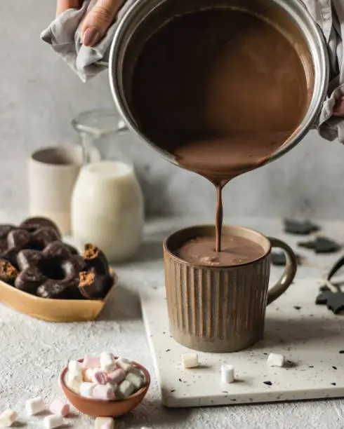 Photo of Cup of hot chocolate poured on bright background with cookies and marshmllow