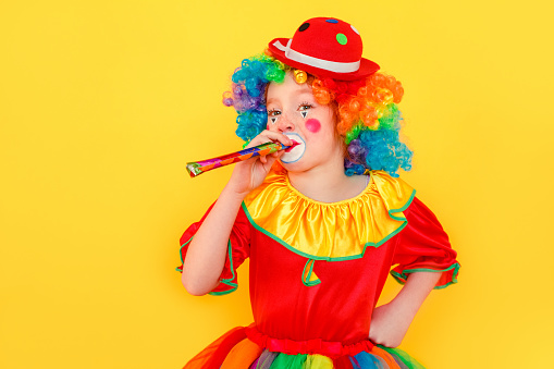 Portrait of little girl wearing clown suit, holding pipe. Studio shot, isolated on yellow background