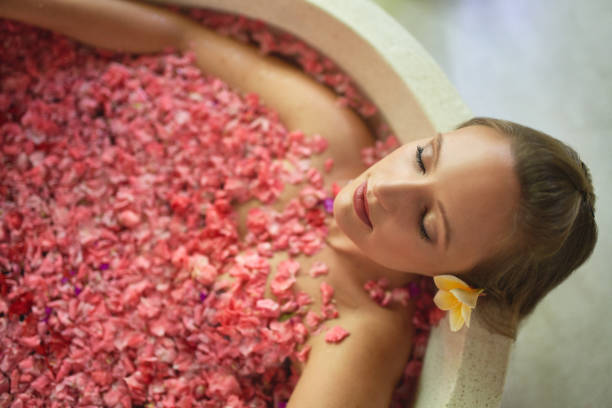 Overhead shot of natural millennial woman in luxurious spa bathtub filled with flower petals in tropical resort and wellness centre stock photo