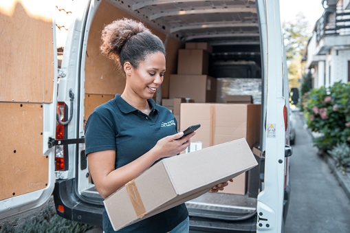 Portrait of an African American woman using phone in front of the delivery van
