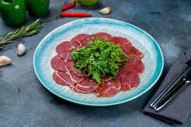 Beef carpaccio with arugula on blue plate Beef carpaccio with arugula on blue plate carpaccio parmesan cheese beef raw stock pictures, royalty-free photos & images