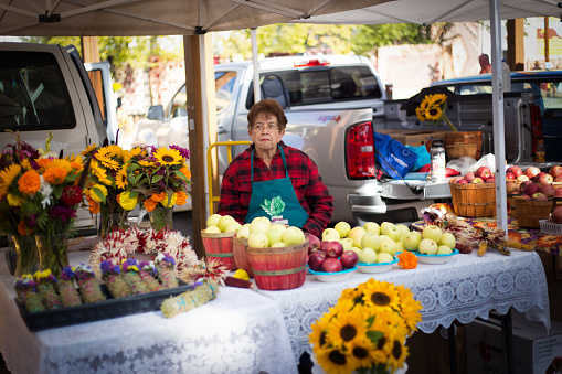 Santa Fe, NM: A woman sits with flowers and baskets of apples at Santa Fe’s Saturday Farmer’s Market.