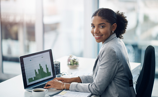 Shot of a young businesswoman using a laptop with graphs on it in a modern office
