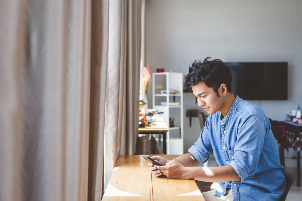 jeune homme beau utilisant le téléphone intelligent à la maison, homme tapant un message de sms et dispositifs mobiles de travail, concept de technologie de mode de vie de personnes - technology typing male beauty asian and indian ethnicities photos et images de collection