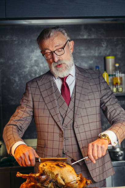 istock Old-aged handsome man in formal expensive suit cutting out roasted chicken 1184789718