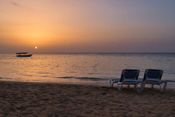 istock Two beach chairs and boat at sunset 1184790622