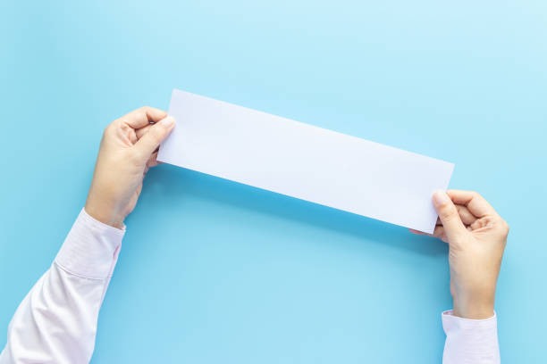 fermer les mains en tenant vide blanc blanc papier horizontal pour le dépliant ou l'invitation maquette d'isolement sur un fond bleu. - book reading white women photos et images de collection